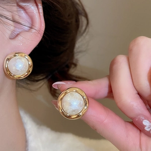 Close-up of gold-plated pearl stud earrings with textured geometric rim on model ear