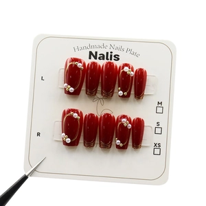 Elegant red press-on nails set with gold trim and white pearls for New Year luxury