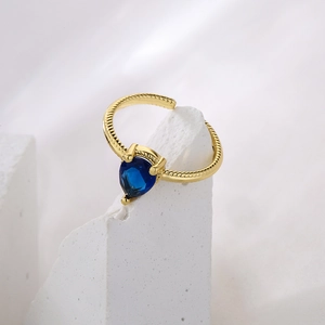 Adjustable gold ring with a blue teardrop stone and spiral texture on a stone background
