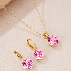Close-up of gold-plated necklace and drop earrings set with heart-shaped pink crystals