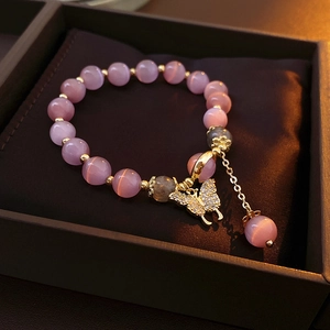 Détail du bracelet en perles œil-de-chat avec pendentif papillon et pompons dorés