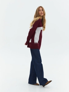 Detail view of burgundy knit sweater with white side lettering paired with wide-leg jeans