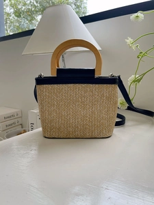 Detail of straw bucket bag with wooden handle, black strap and beige woven texture