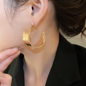 Nahaufnahme eines Models mit goldfarbenen C-förmigen Creolen mit glänzendem Metallfinish