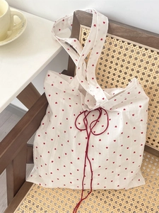 White canvas tote bag with red heart pattern and drawstring on a vintage chair