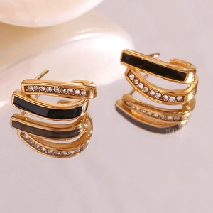 Detailed macro view of gold U-shaped earrings with black enamel and white rhinestones