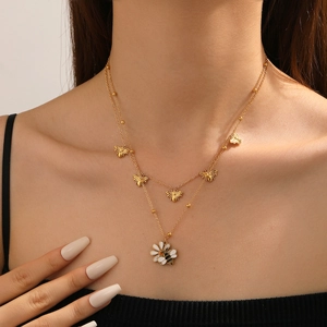 Dettaglio di una collana dorata a strati con piccoli ciondoli a ape e fiore bianco