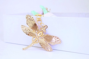 Detailed view of a golden metal dragonfly keychain with textured wings on a box