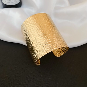 Macro shot of wide gold cuff bracelet featuring irregular hammered honeycomb texture