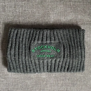 Detail eines breiten Rippstrick-Stirnbands in Dunkelgrau mit grüner Stickerei