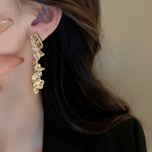 Detail of elegant gold irregular fluid drop earrings worn by a model in soft lighting