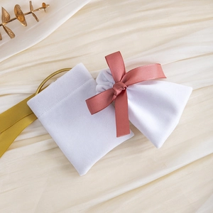Detailed view of white velvet drawstring pouches with elegant pink ribbon bow on beige fabric