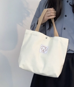 Detail of canvas handbag featuring a lovable cartoon dog patch and metal snap button