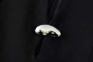 Macro shot of silver organic shaped metal button on black stand-up collar dress fabric