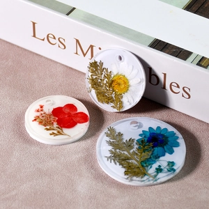 Vue détaillée de pendentifs circulaires en résine faits main avec fleurs séchées colorées
