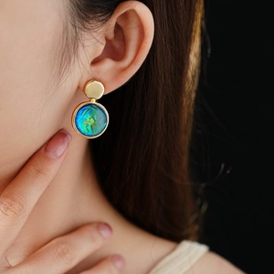 Close-up of model wearing round teal resin stud earrings with elegant gold metal frames