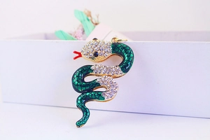 Close-up of green enamel snake pendant with white crystals on a gold-plated base