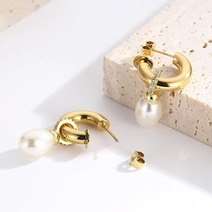 Élégantes boucles d'oreilles créoles dorées avec perles et zircon sur pierre beige