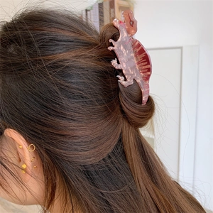 Detail view of pink dinosaur acetate hair claw clip worn on a woman's bun hairstyle