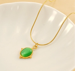 Détail d'un collier chaîne serpent dorée vintage avec pierre verte ovale sur un plat en céramique