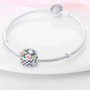Detalle de pulsera de cadena de serpiente plateada con dije de esmalte floral y corazones