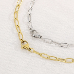 Close-up of gold and silver paperclip chain necklaces with lobster clasps on fabric