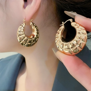 Detail shot of chunky gold hoop earrings with textured interlaced woven metal pattern