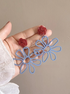 Detailed view of oversized resin flower earrings with red rose and blue hollow pendant