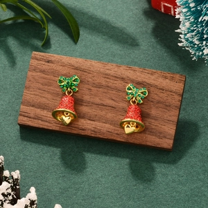 Close-up of red Christmas bell earrings with green zircon bows on a festive wood base