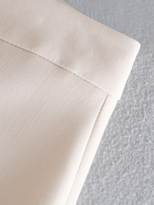 Macro shot of cream woven fabric texture and stitching details on straight-leg trousers
