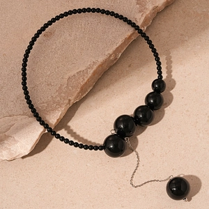 Détail d'un collier vintage à perles noires avec sphères en dégradé sur pierre beige