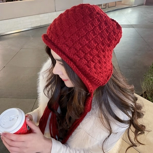 Detail of red crochet knit earflap hat with thick checkered texture and fringe scarf