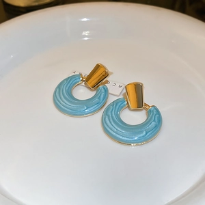 Détail des boucles d'oreilles bleu clair ondulées avec accents dorés sur assiette céramique