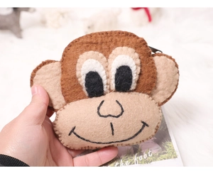 Close-up of handmade brown felt monkey coin purse held against a soft plush background