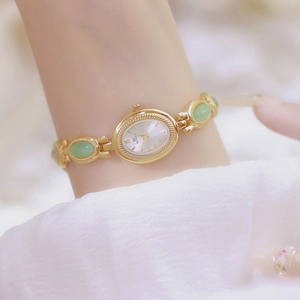Close-up of elegant gold watch featuring green jade-style link strap on a wrist