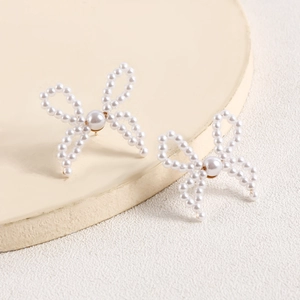 Detail of handcrafted pearl bow earrings with golden pin on a textured neutral background