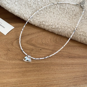 Détail du collier de perles avec pendentif poney en émail bleu sur tissu doux