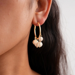 Detail of bohemian gold hoop earrings with white marble-textured stone beads on a model