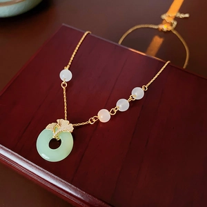 Detail of light green glass pendant with golden ginkgo leaf clasp on wood surface