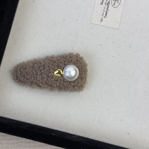 Close-up of brown plush drop-shaped hair clip featuring a white pearl and gold bead