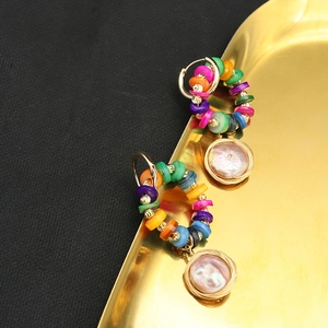 Detailed close-up of colorful bead earrings with pearl charms on a golden metal tray