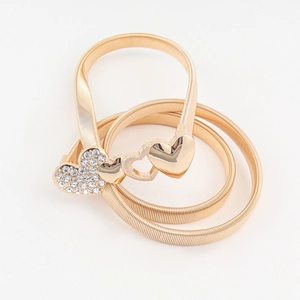 Detail view of a gold elastic metal belt featuring a sparkling rhinestone heart buckle
