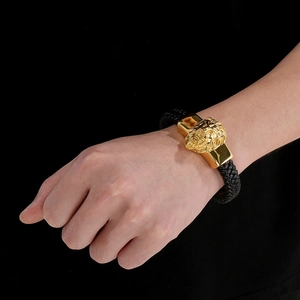 Gros plan d'un bracelet en cuir tressé noir pour homme avec fermoir tête de lion doré au poignet