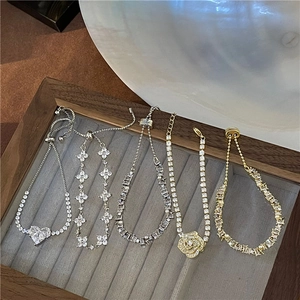 Selection of delicate gold and silver bracelets with heart and floral charms on grey velvet