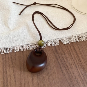 Detail of vintage resin pebble pendant necklace with green cat-eye bead on a wax cord