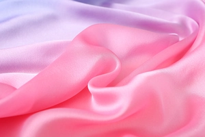 Makroaufnahme von Seidensatin in Rosa-Lila-Verlauf mit weichen Texturfalten