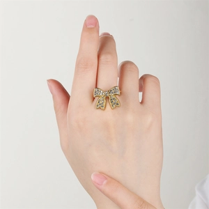 Gold bow-shaped stainless steel ring with pavé diamonds on woman's middle finger