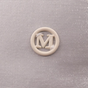Macro detail of the M logo badge sewn on grey high-quality satin baseball cap fabric