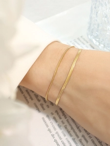 Close-up of gold snake and flat blade layered bracelets on wrist with glossy finish