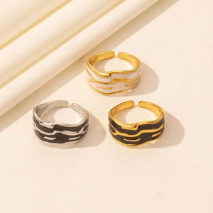 Close-up of enamel wave rings in gold and silver colors on a soft fabric texture
